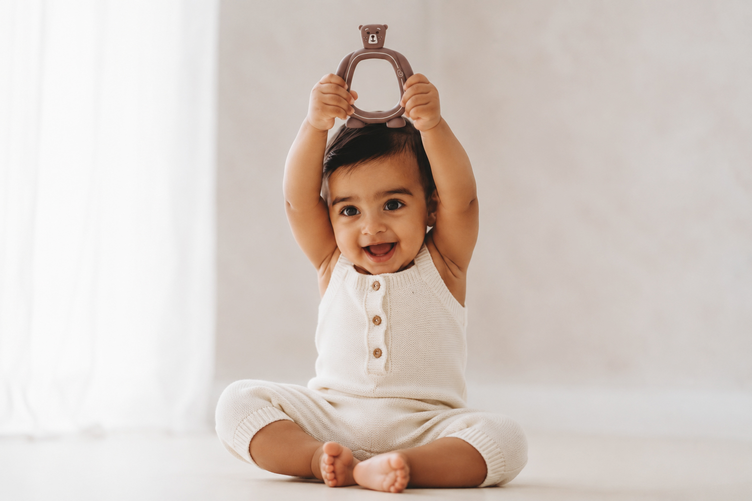 Happy baby holding the Bear Buddy silicone teether above their head, smiling